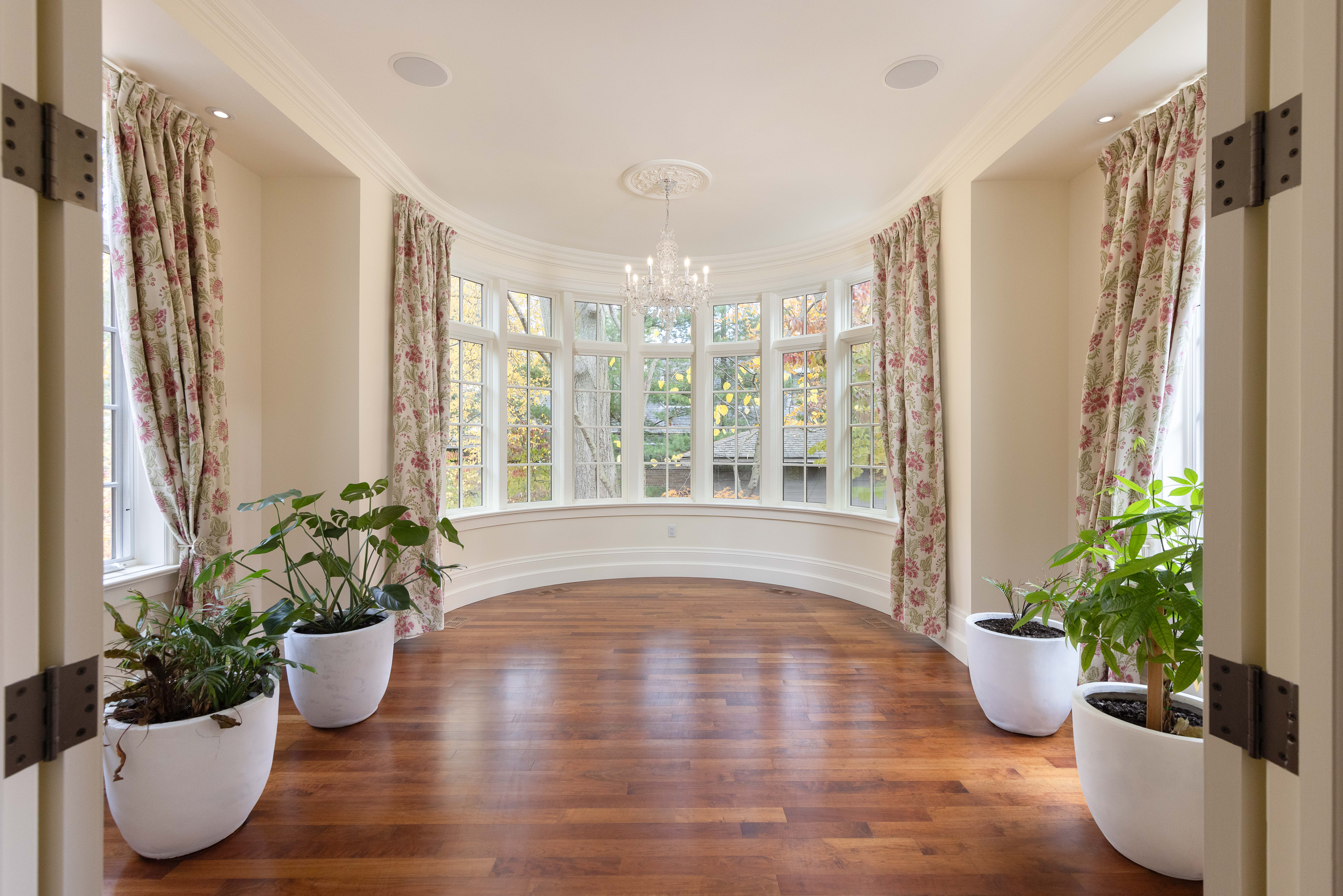 Bright sunroom with large windows, wooden floor, and potted plants