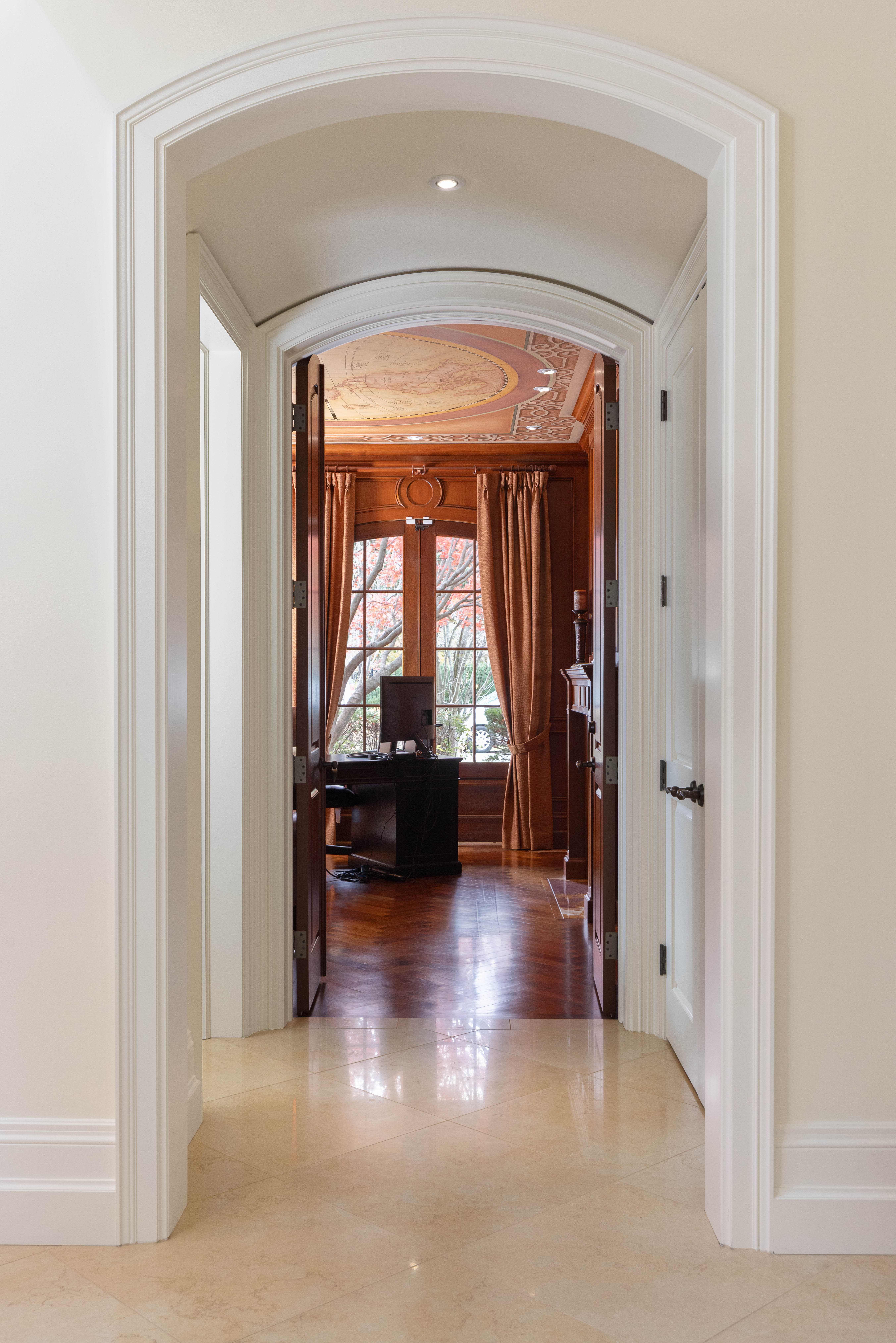 Arched hallway leading to a wooden office with large windows and curtains