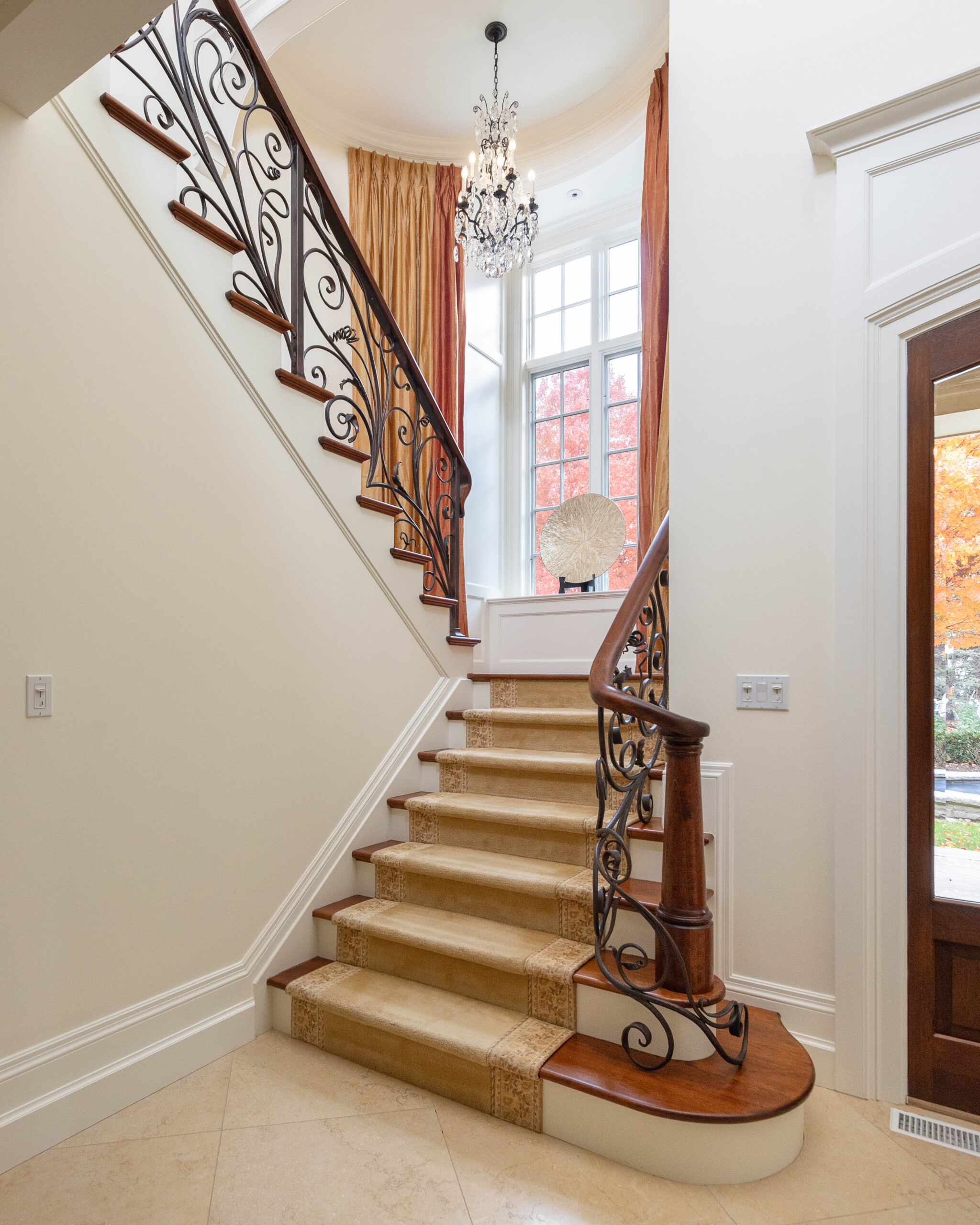 Elegant staircase with ornate railing and chandelier in a bright foyer