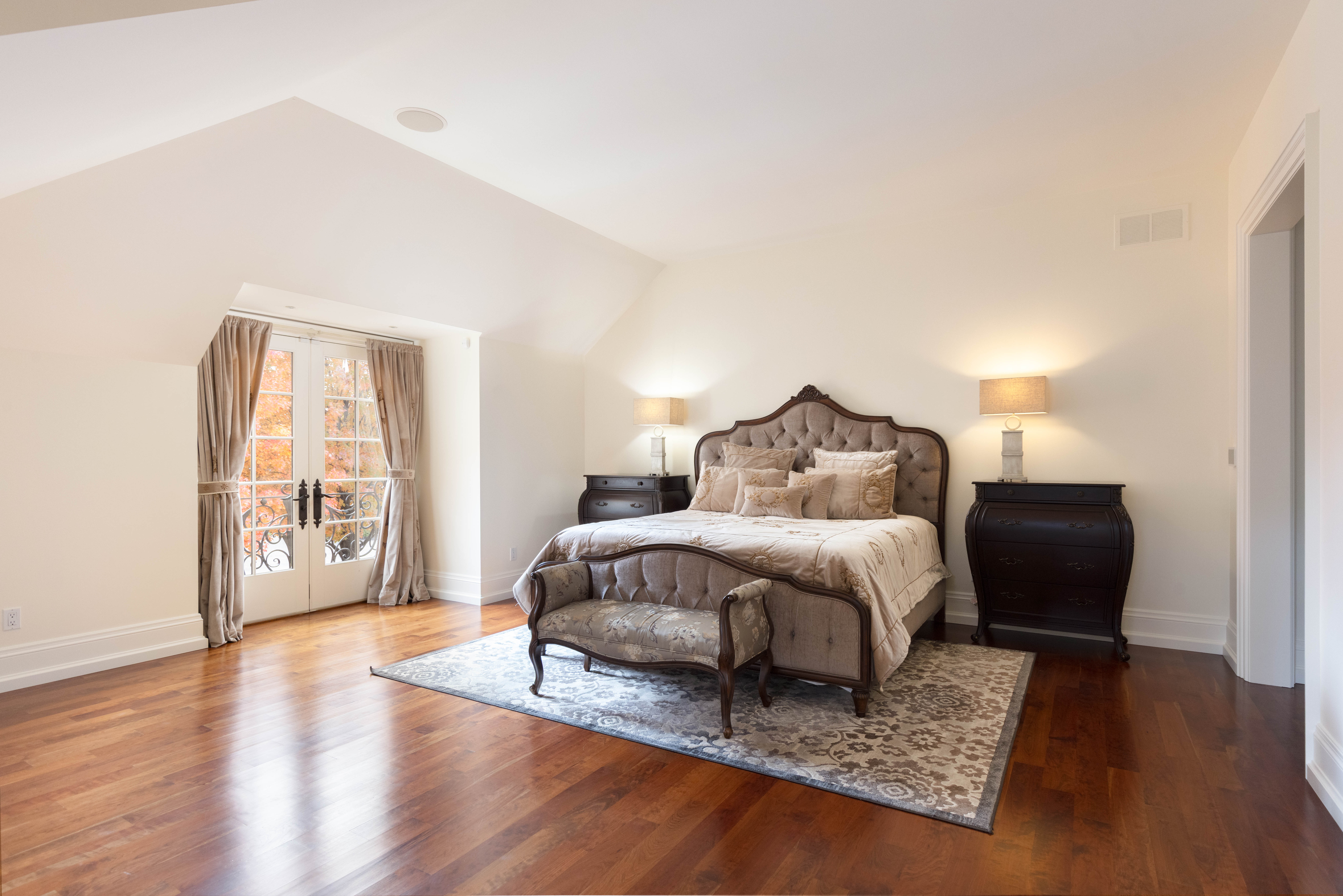 Elegant bedroom with a large bed, wooden floors, and natural light.