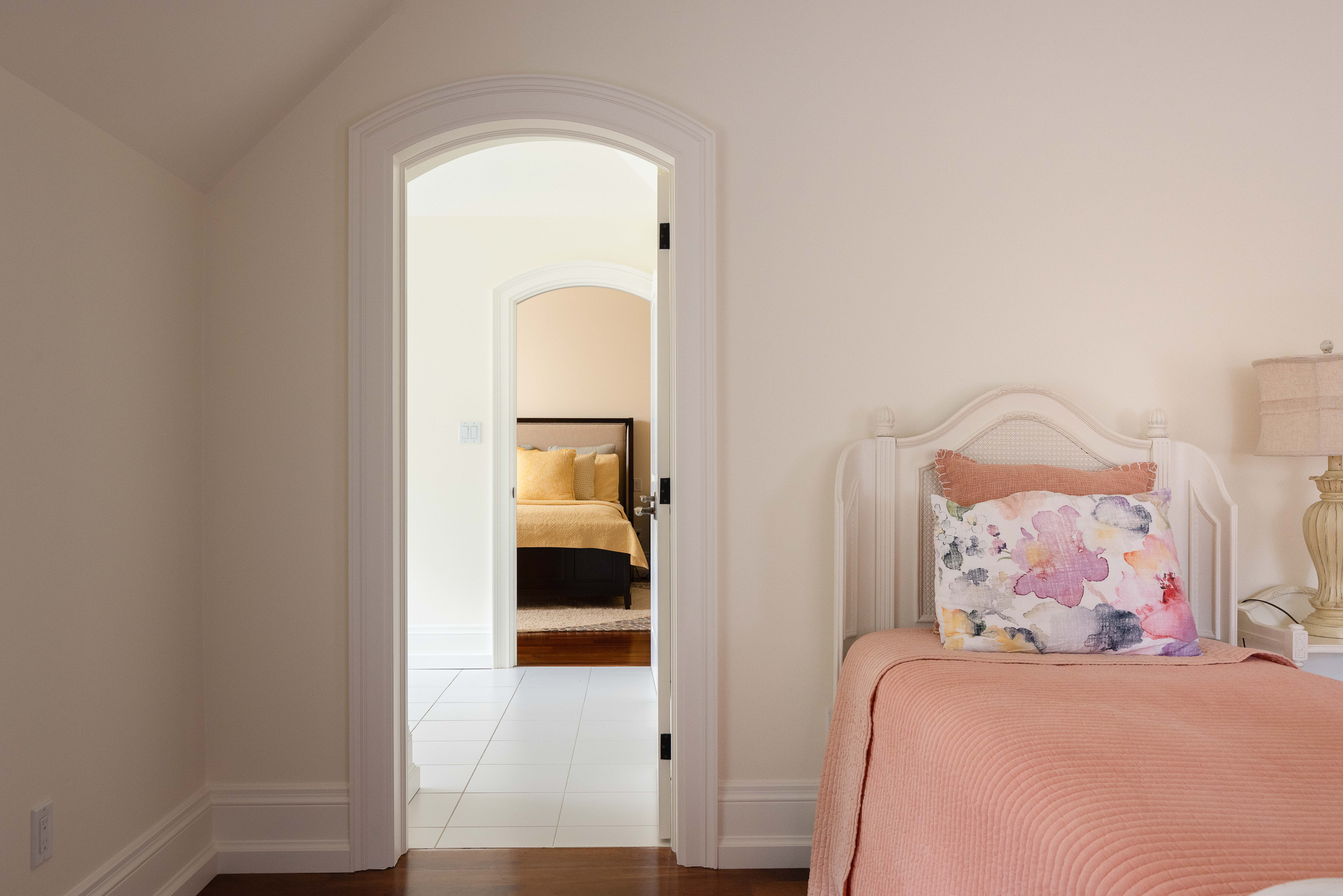 Cozy bedroom with a pink blanket and floral pillow, doorway to another room visible