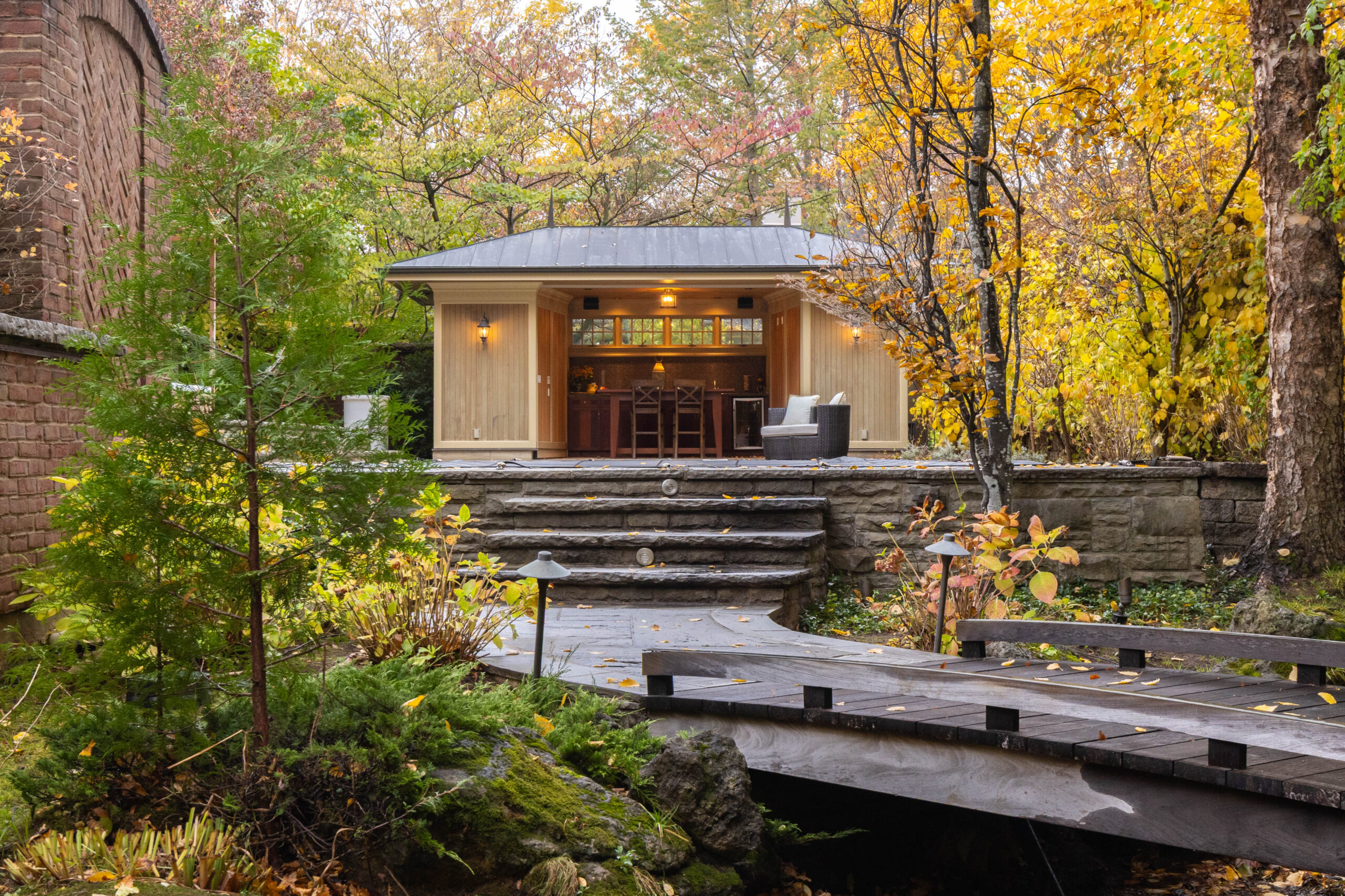 Modern outdoor structure surrounded by autumn foliage and a wooden bridge
