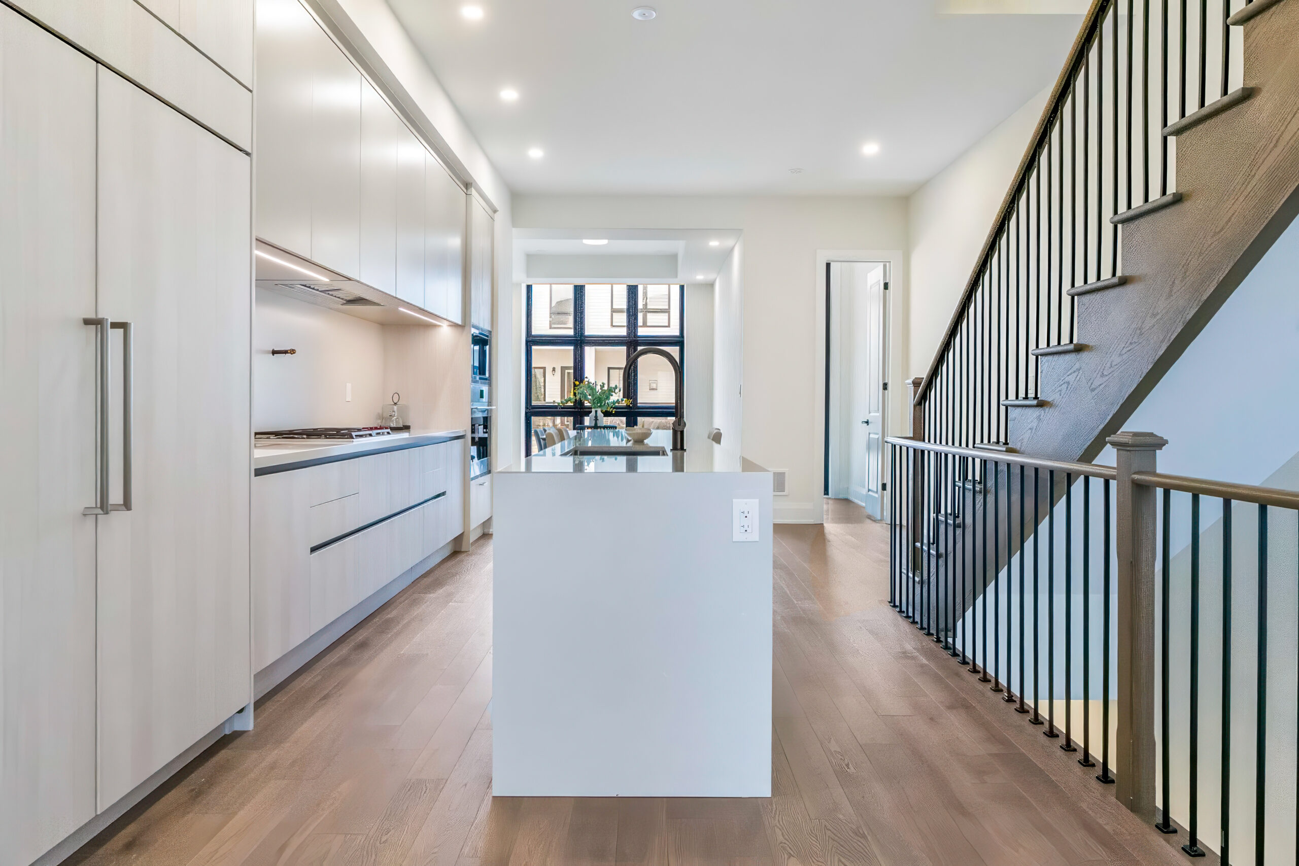 Modern kitchen with an island, wooden flooring, and staircase in background