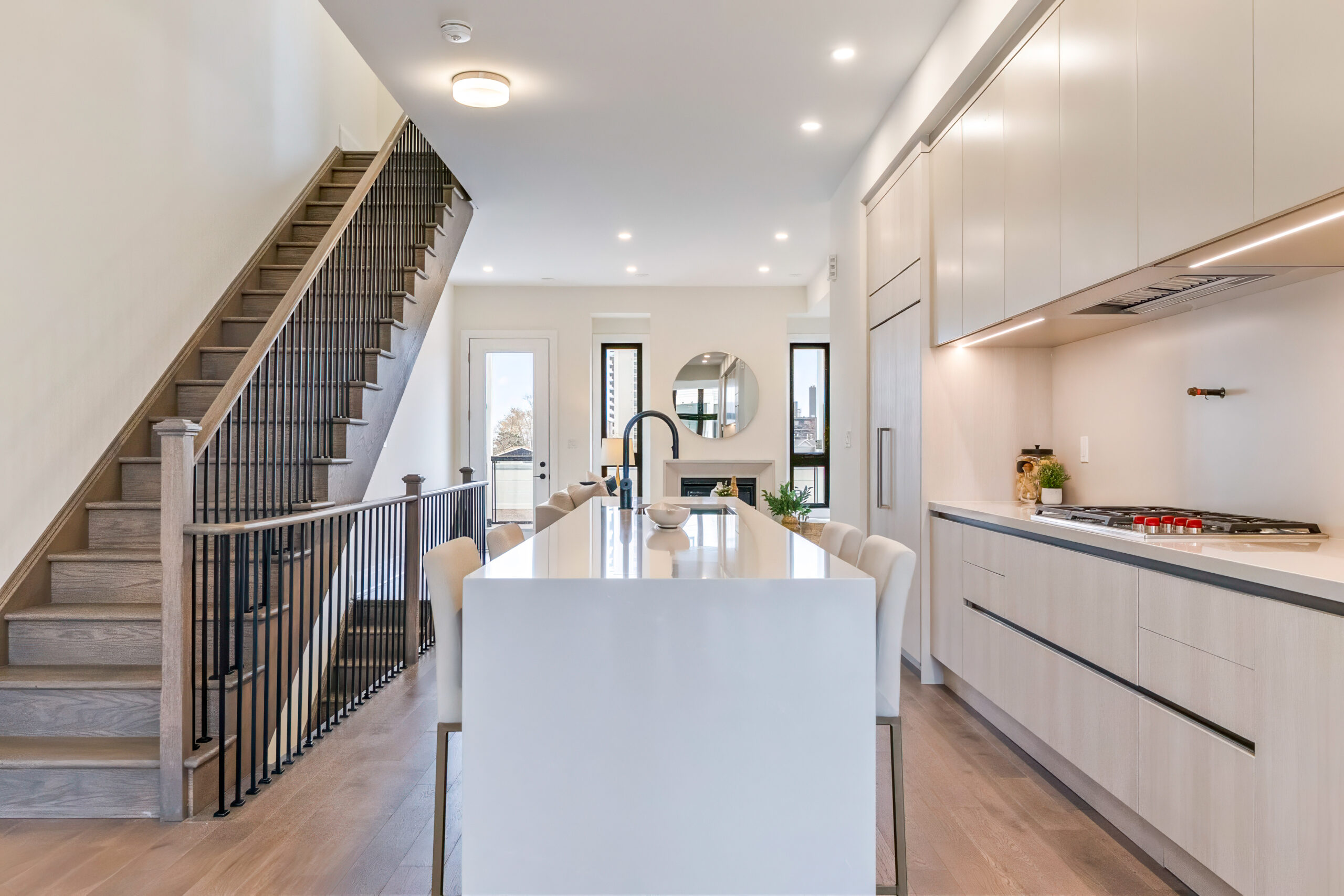 Modern kitchen with white cabinetry and a large island, featuring a staircase in the background