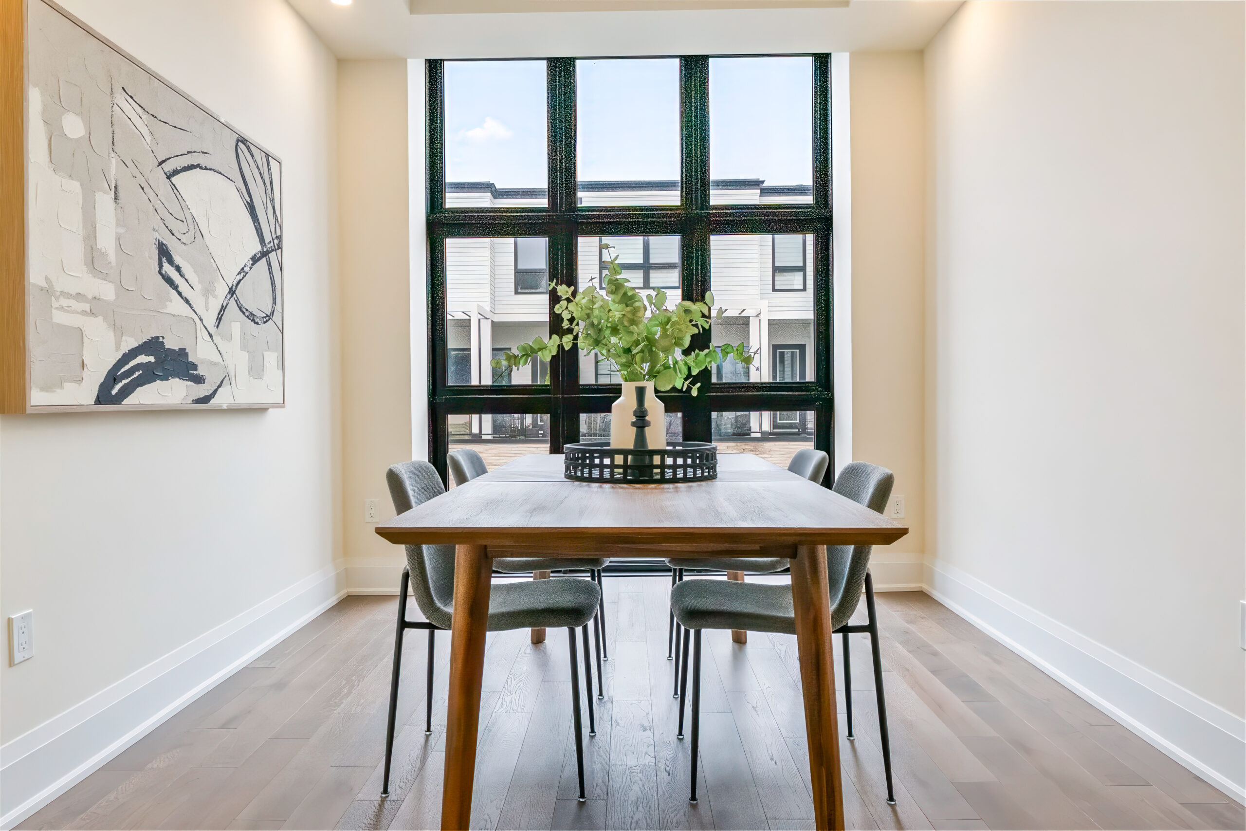 Modern dining area with a wooden table and stylish chairs, large windows, and artwork