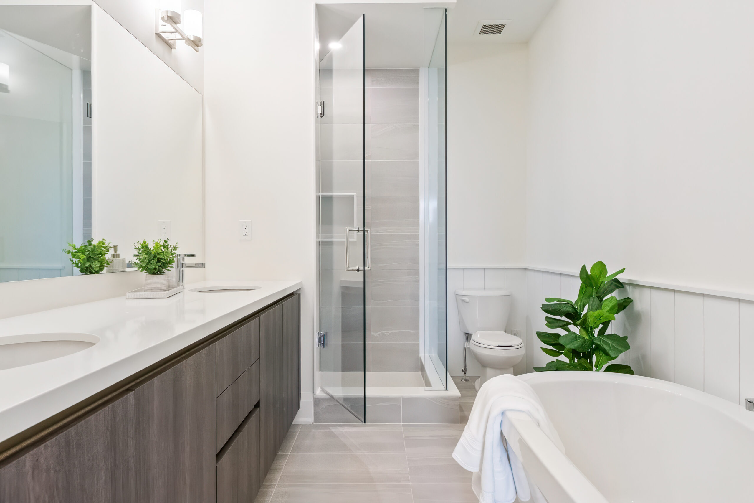 Modern bathroom featuring a glass shower, freestanding tub, and greenery.