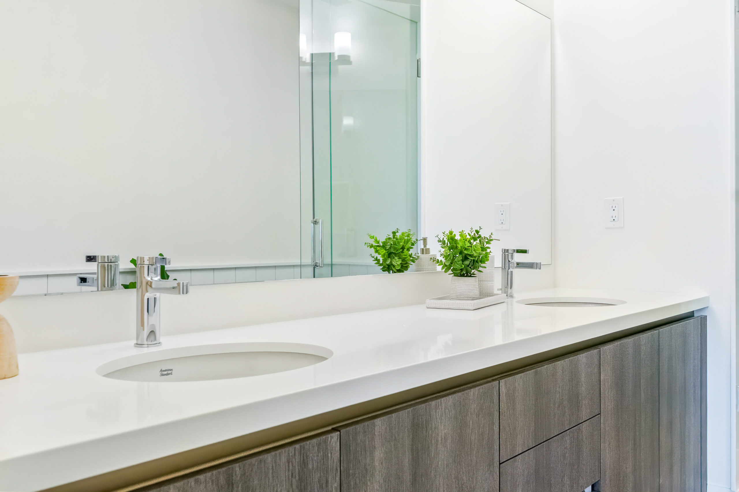 Modern bathroom with dual sinks, wooden cabinetry, and greenery accents