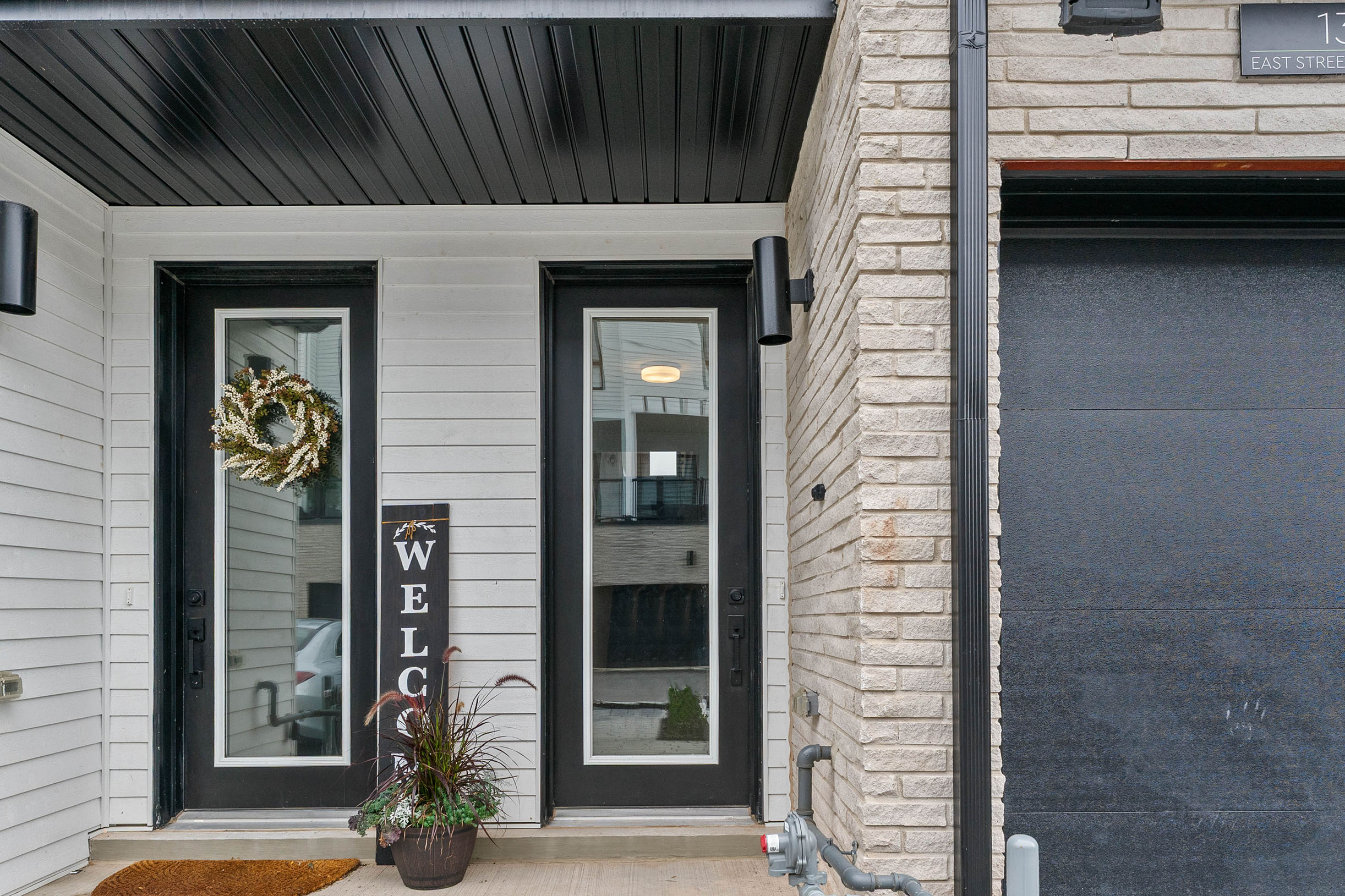 Modern entrance with double doors, welcome sign, and potted plant
