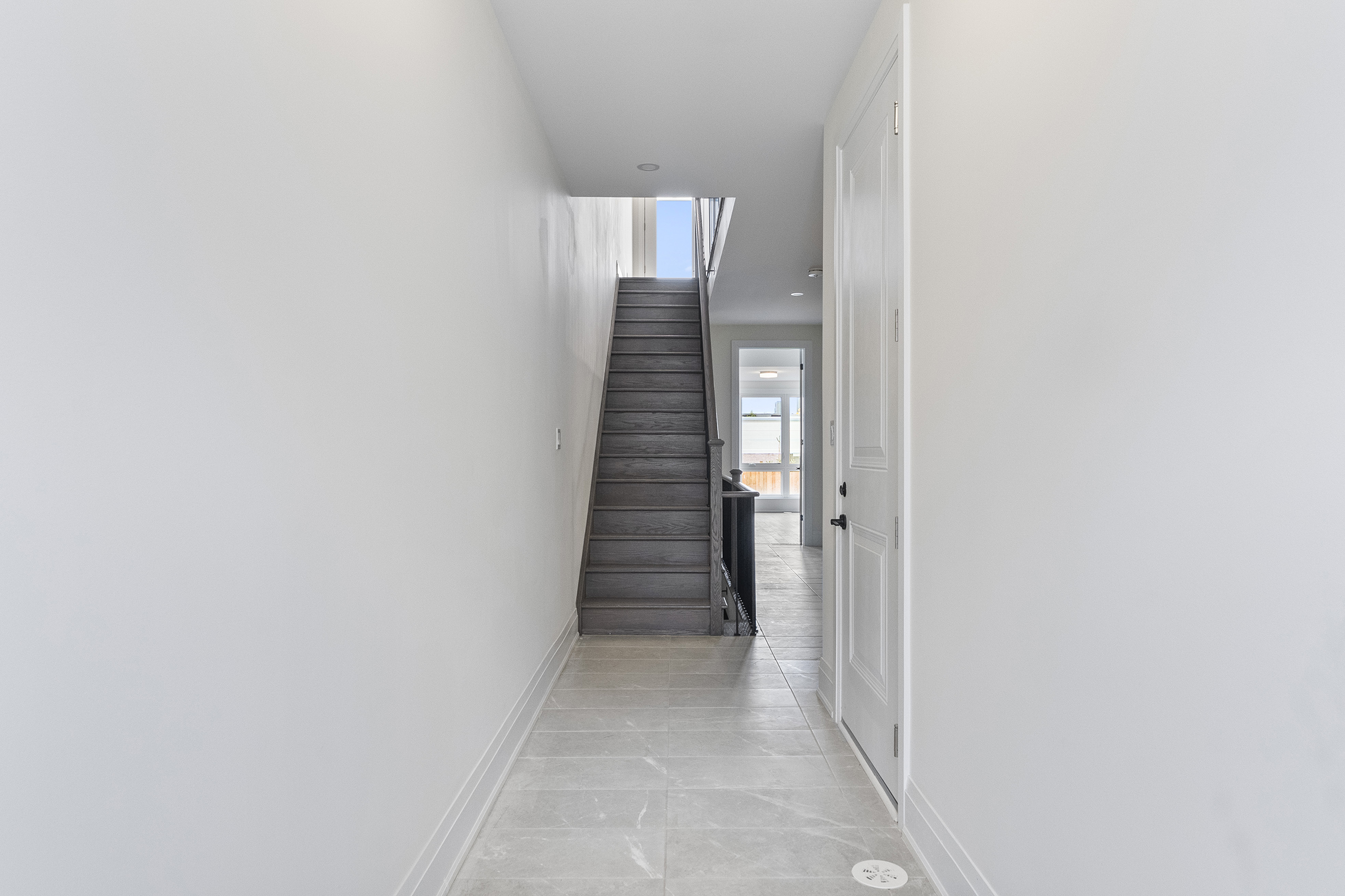 Bright hallway leading to a staircase with light-colored walls and flooring