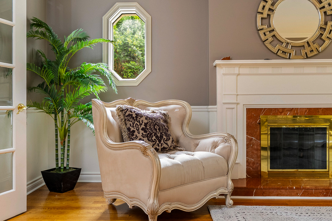Elegant armchair with decorative pillow beside a fireplace and potted plant