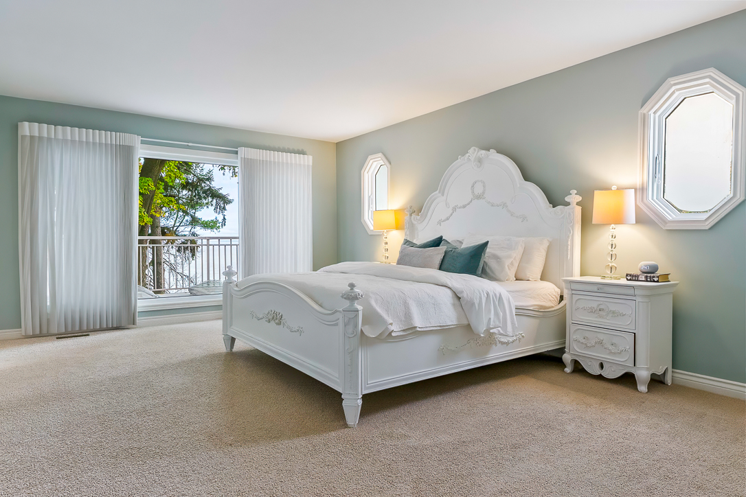 Bright bedroom with white furniture and large windows overlooking greenery