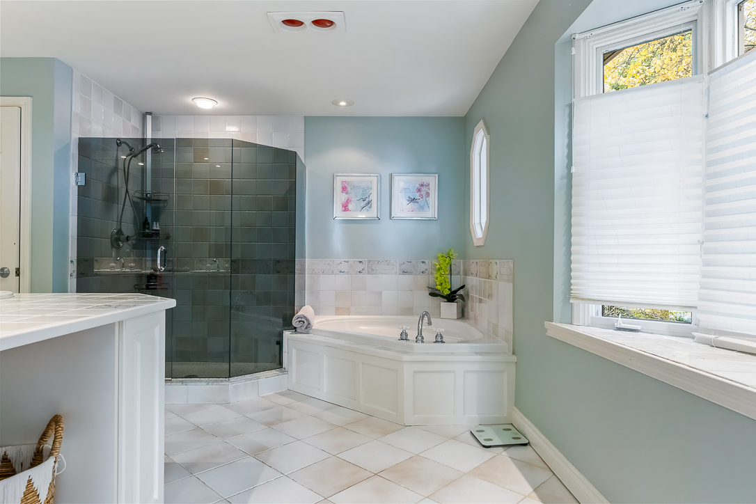 Spacious bathroom with a glass shower, bathtub, and light blue walls