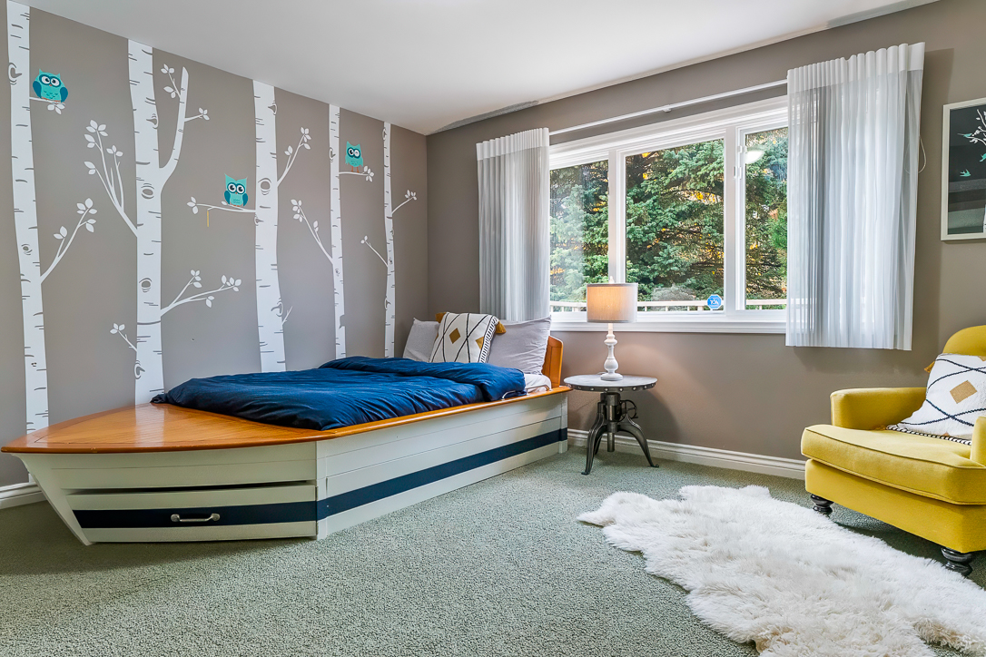 Cozy bedroom with a boat-shaped bed, yellow chair, and tree-themed wall decor