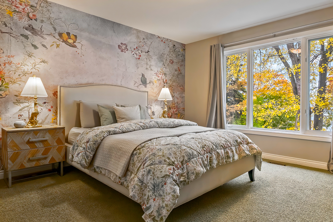 Cozy bedroom with floral wallpaper and large window overlooking autumn trees