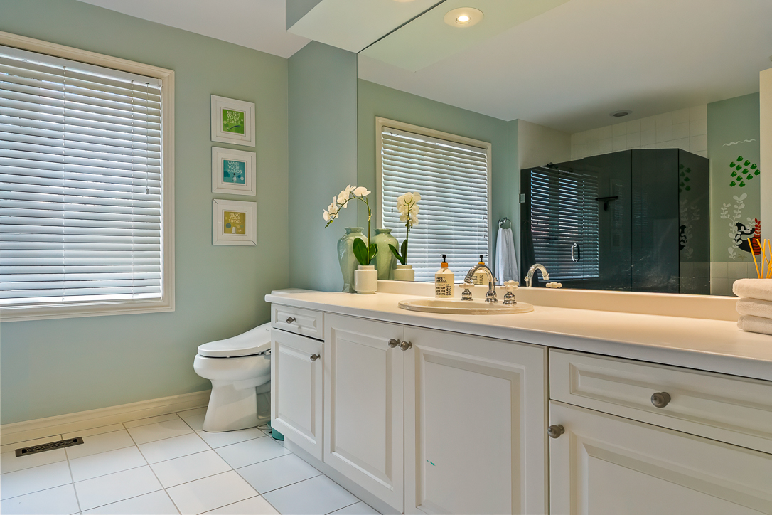 Modern bathroom with light blue walls, white cabinetry, and natural light.