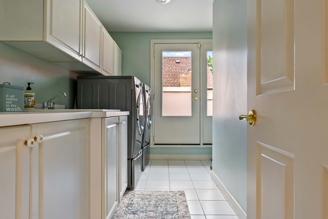 Bright laundry room with white cabinets and stainless steel appliances