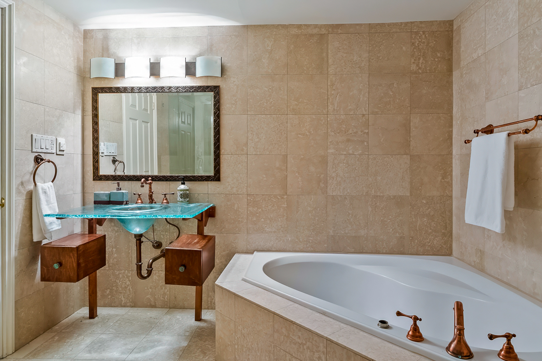 Luxurious bathroom featuring a glass sink, wooden vanity, and a large bathtub