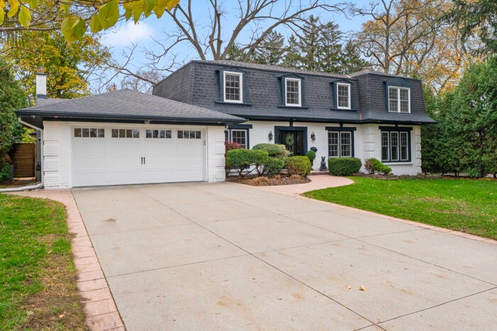 Two-story house with a black roof and garage, surrounded by greenery
