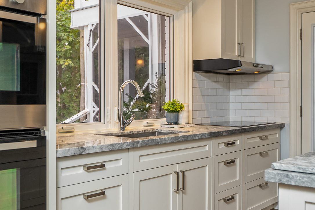 Modern kitchen with white cabinetry, granite countertops, and a window view.