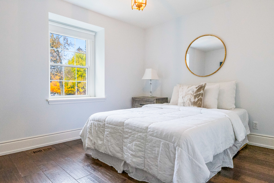 Bright bedroom with a white bed, lamp, and large window.