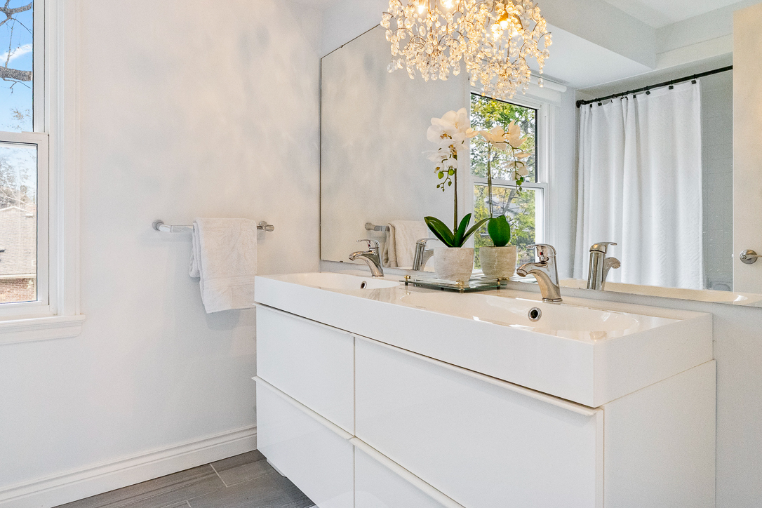 Modern bathroom with white cabinetry, a chandelier, and an orchid centerpiece