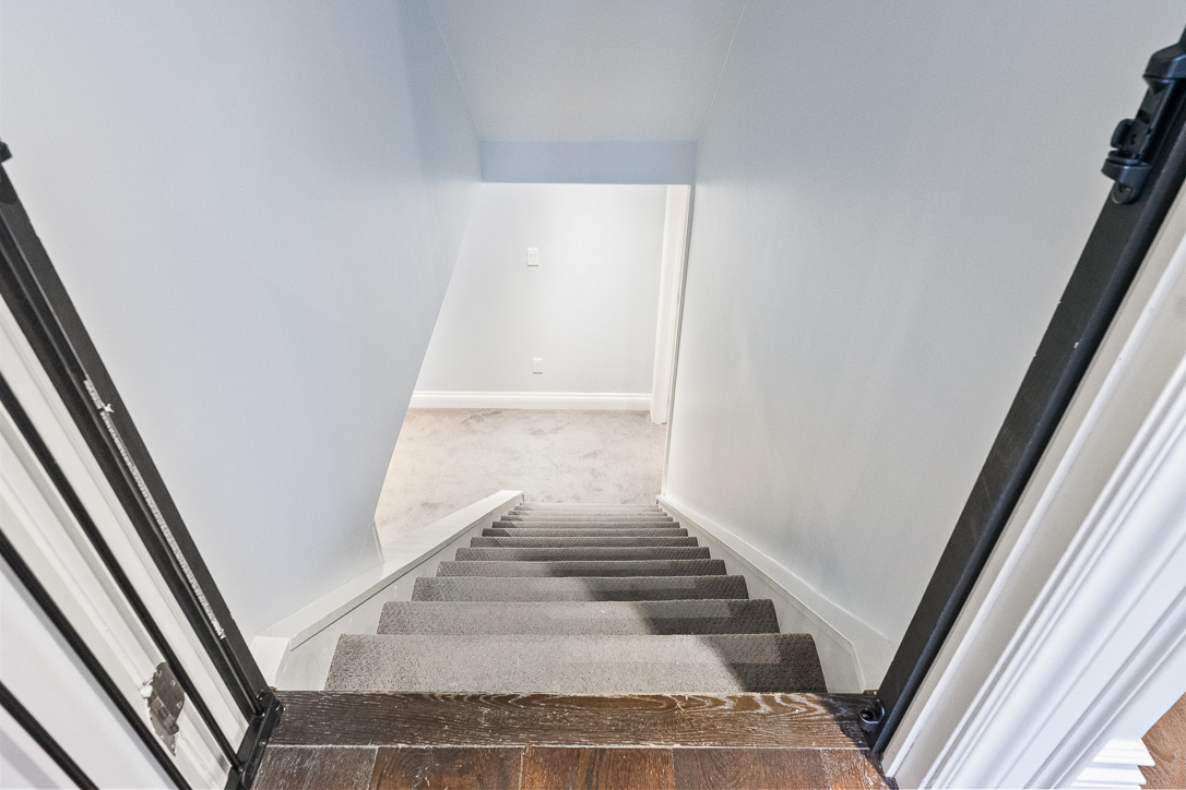 View down a staircase with light-colored walls and carpeted steps