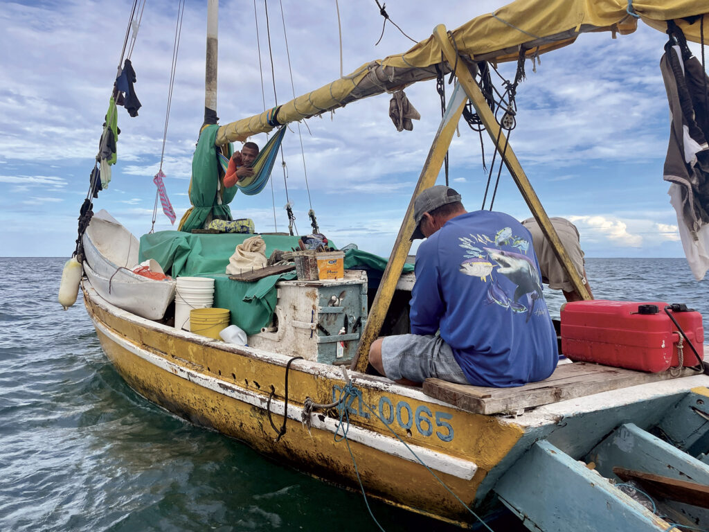 A local fisherman at Ray Cay prepares to clean his catch while his crew takes five in the hammock.