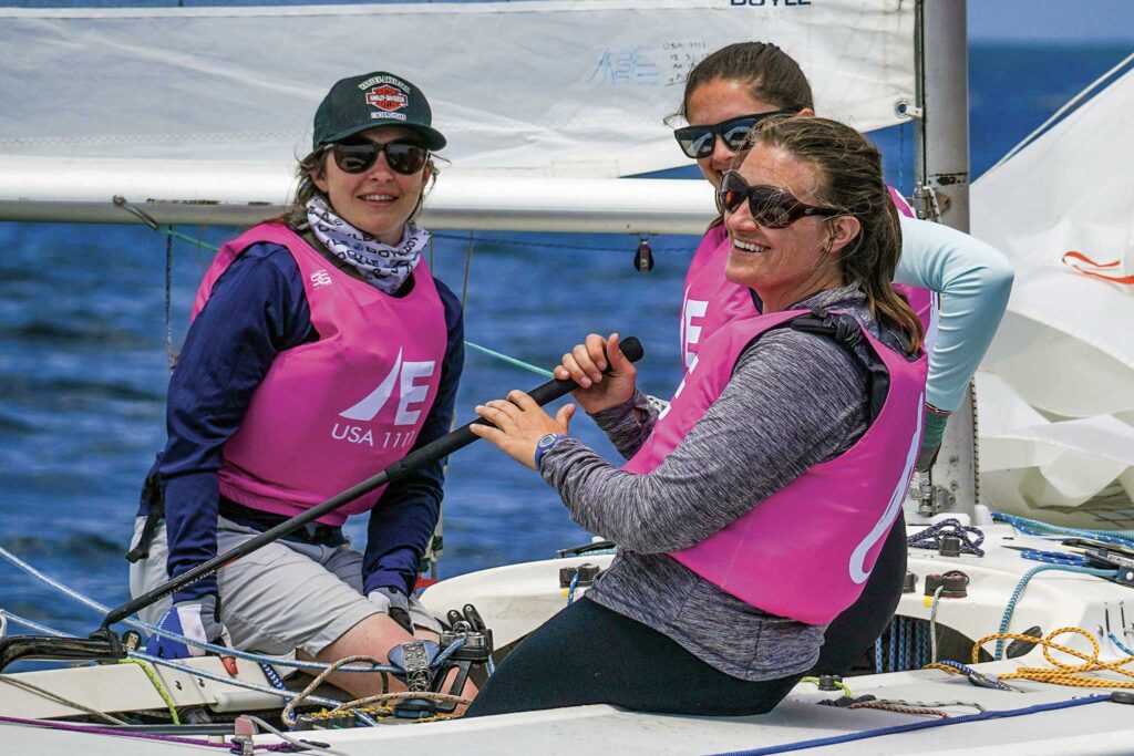 Three women in pink life jackets are sailing a boat on the water.