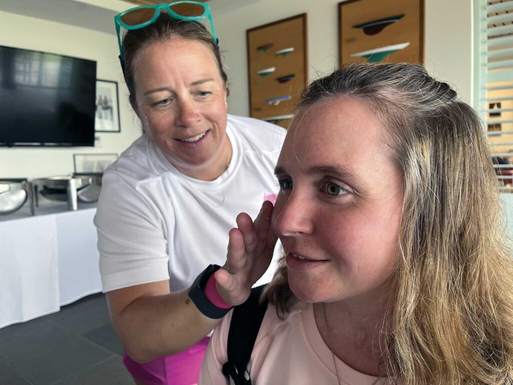 A close-up of two women in a room. One is touching the other's face.