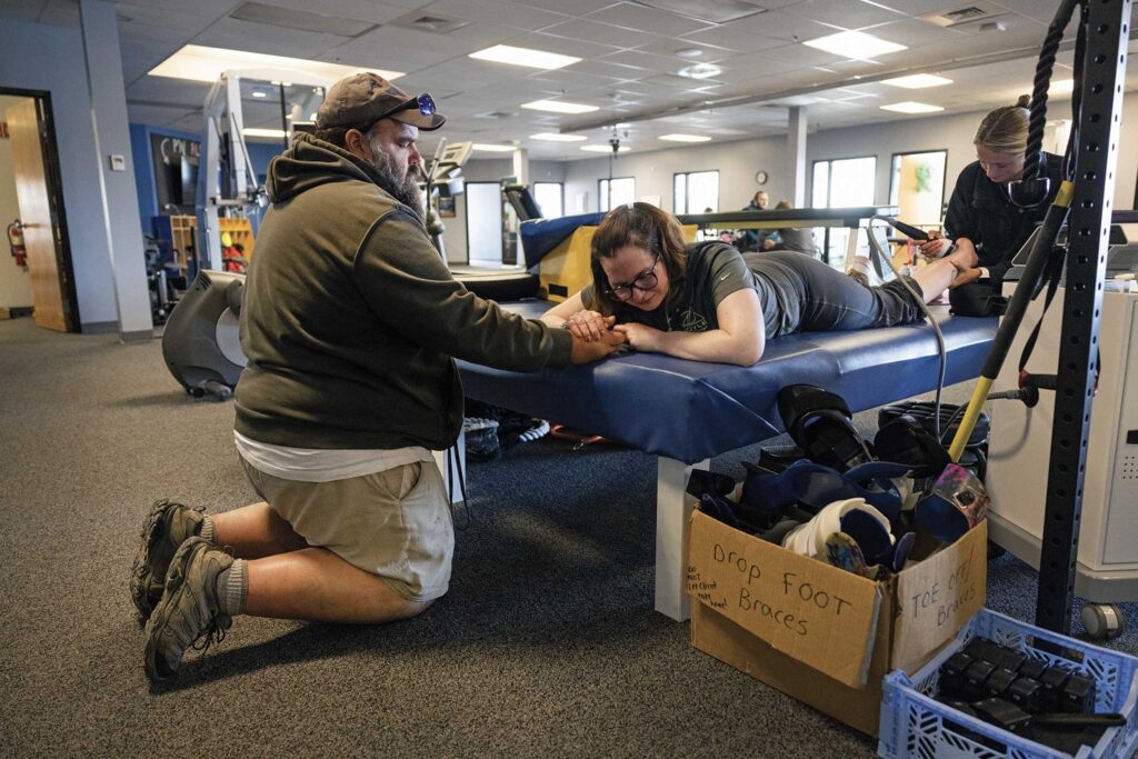 A man, assisting a woman on a bench during physical therapy.