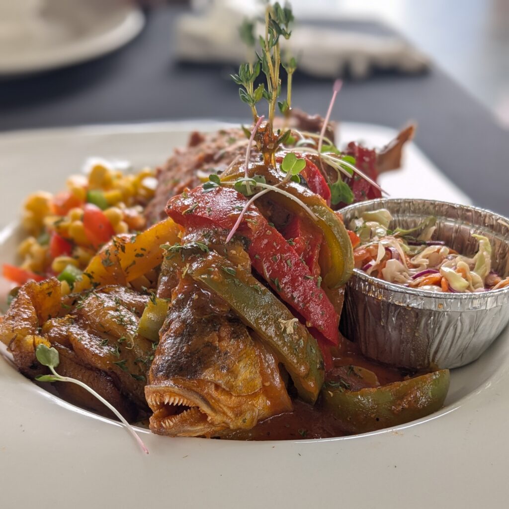 A fish on a plate with peppers, cole slaw, and plantains