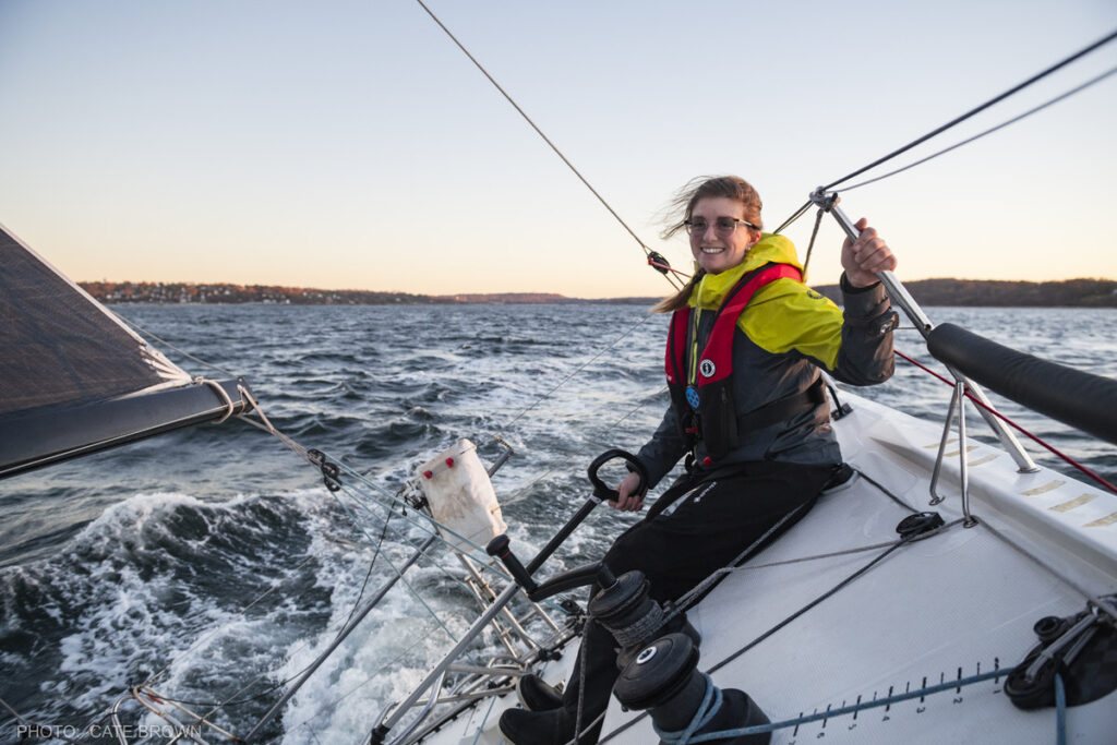A sailor smiling while steering a boat by tiller.