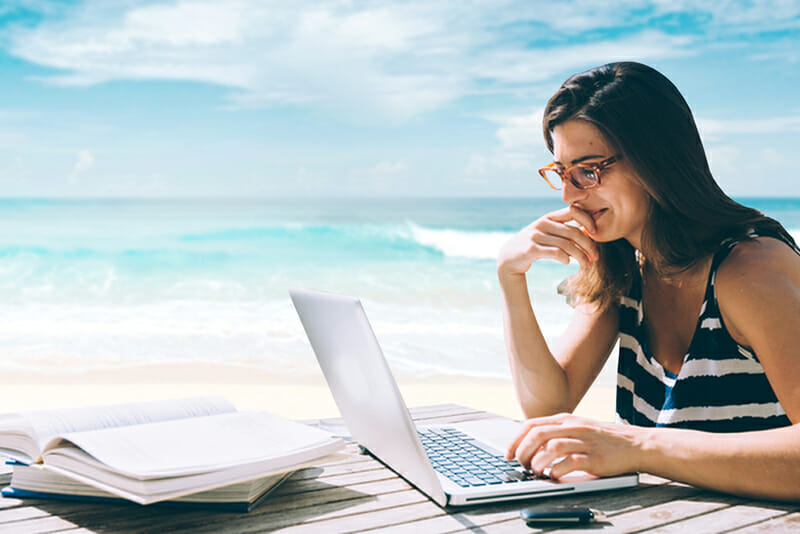 A woman works at her laptop on the beach.