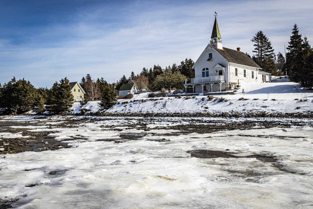 a white building with a steeple on a hill with trees and a river