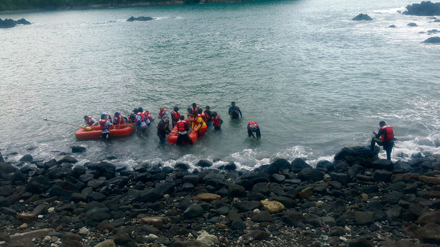 A group of people on a rocky shore in the water with dinghies.