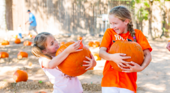 Two girls holding pumpkins.