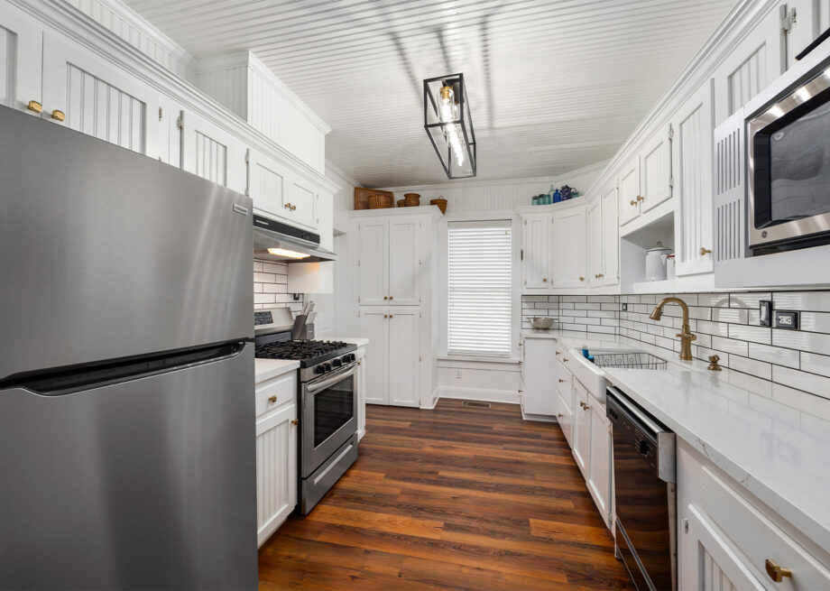 A modern kitchen with white cabinets, stainless steel appliances, a gas stove, subway tile backsplash, and wooden floors.