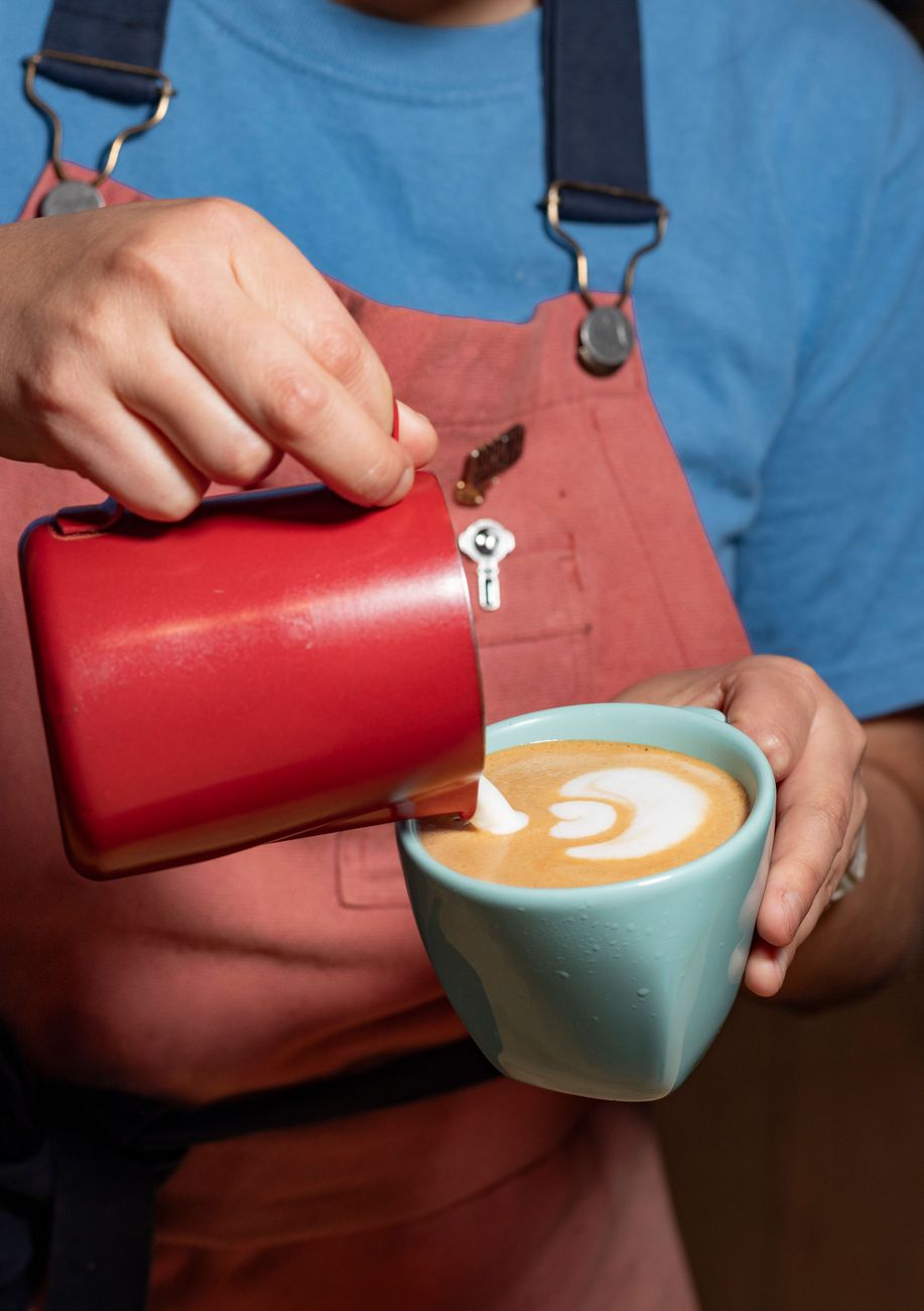 Barista creando intrincadas obras de arte en latte con un vaporizador de leche en un acogedor café.