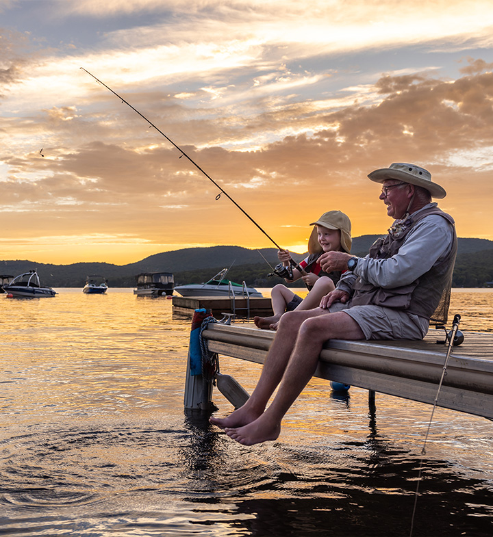 A man and a child fishing from a dock at sunset