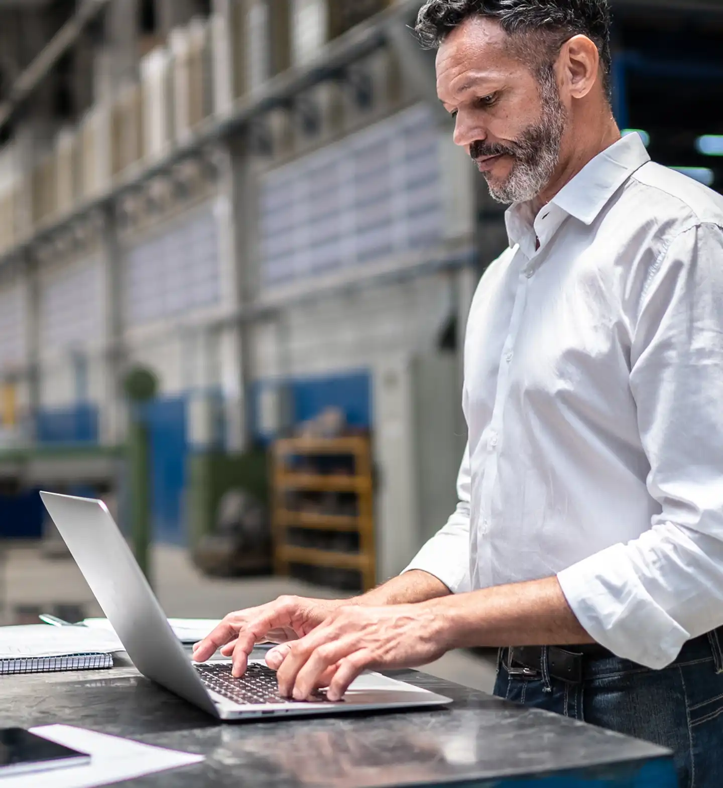 Man in a white shirt working on a laptop in a warehouse setting