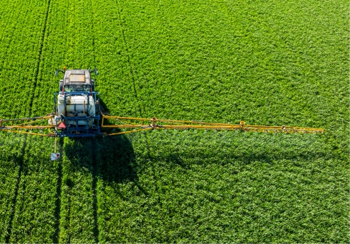 Aerial view of a tractor spraying crops in a green field
