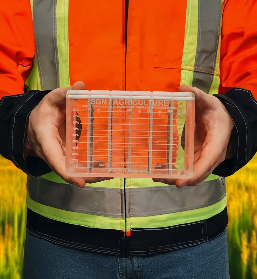 Person in a safety vest holding a transparent container in a field
