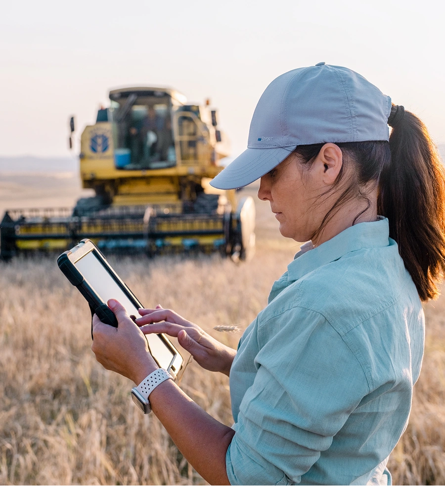 Woman using a tablet in a field with a combine harvester in the background