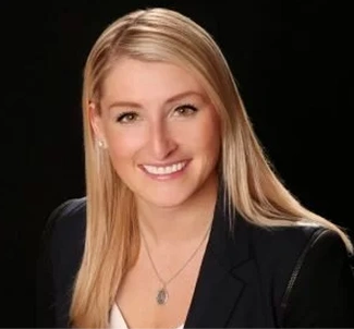 Smiling woman with long blonde hair wearing a black blazer against a dark background