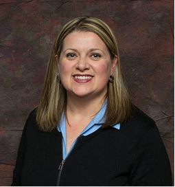 Smiling woman with shoulder-length hair, wearing a black sweater and blue shirt