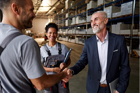 Two workers shaking hands with a businessman in a warehouse setting