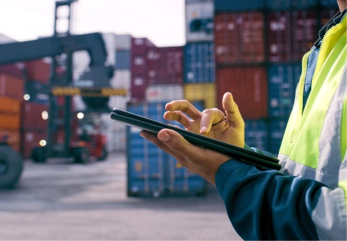Worker using a tablet in a shipping yard with containers in the background