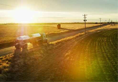 Truck driving along a rural road at sunset, surrounded by fields