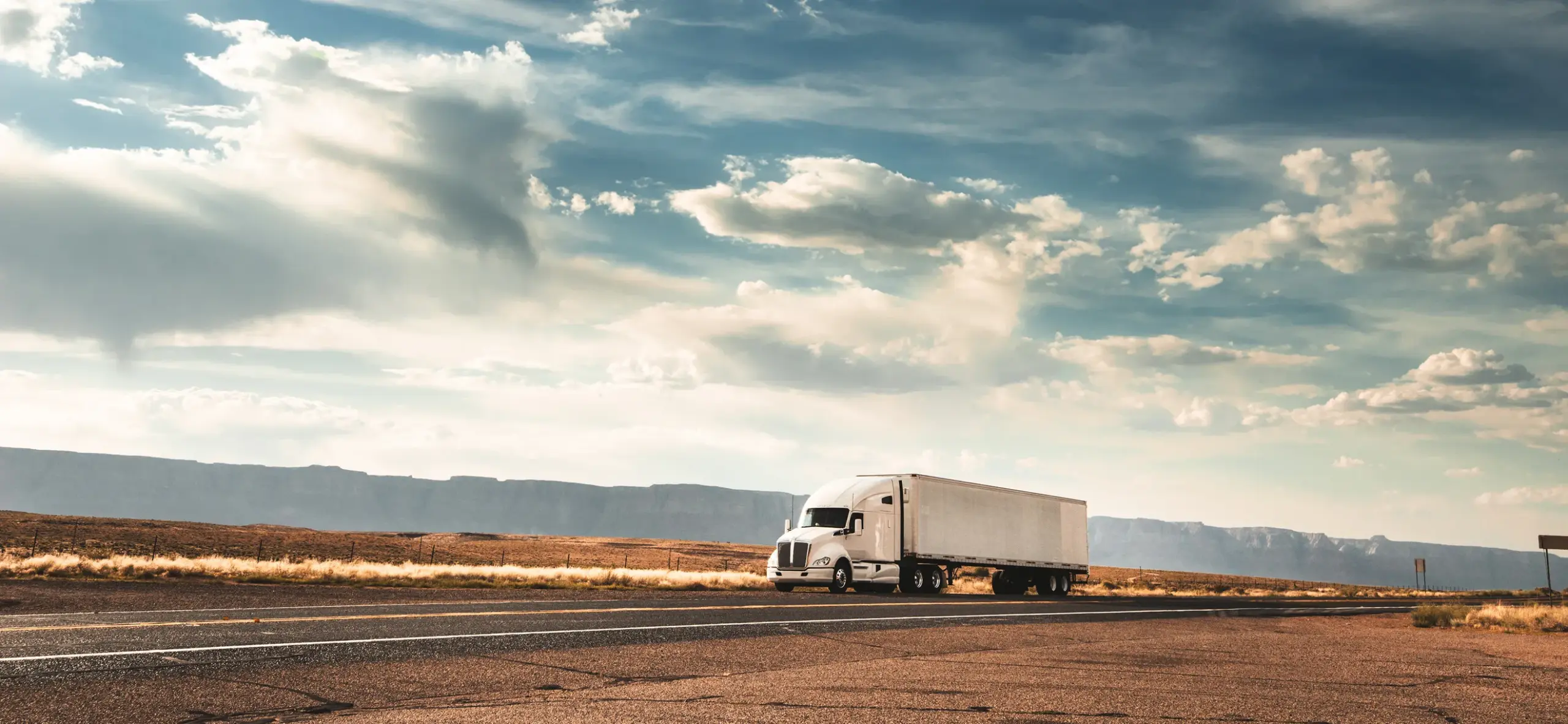 Truck driving on a wide, empty road under a cloudy sky
