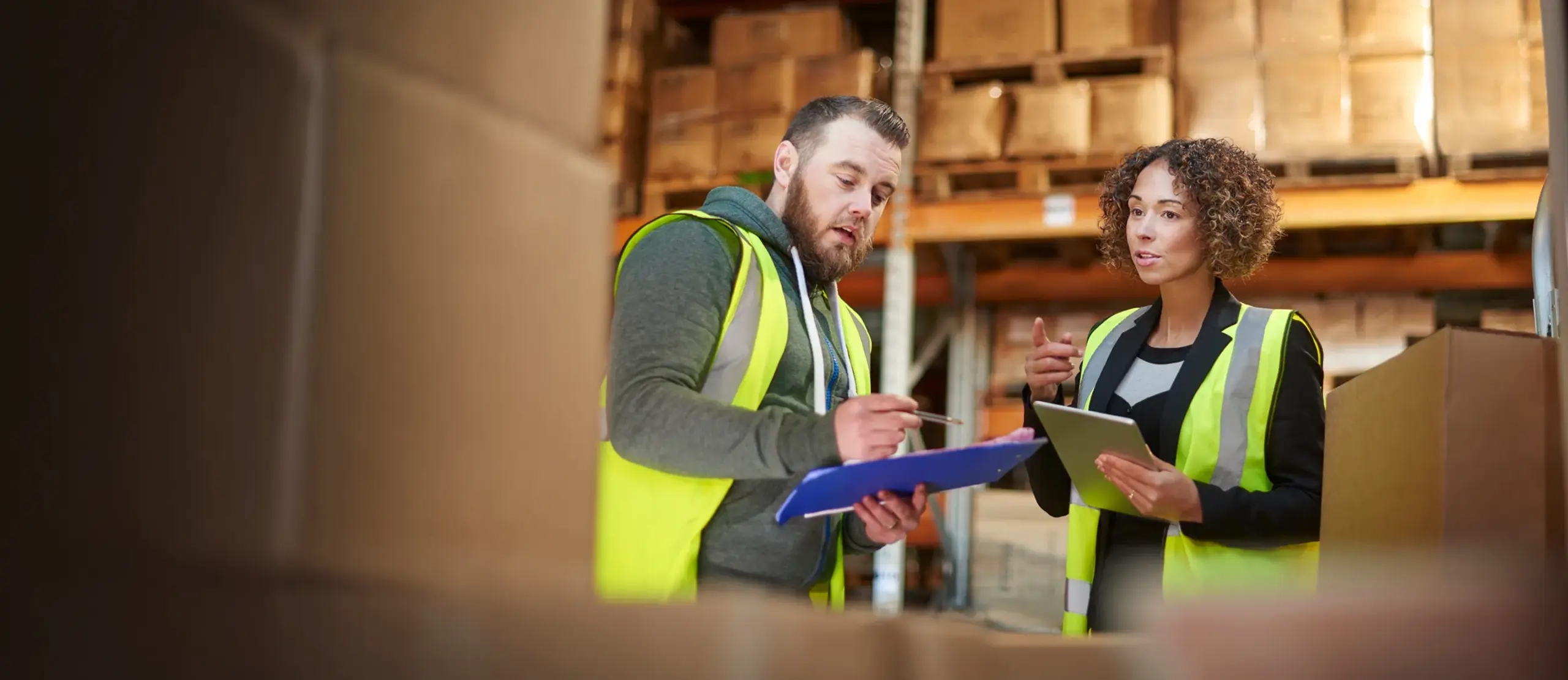 Two warehouse workers discussing inventory with clipboards in a storage area.